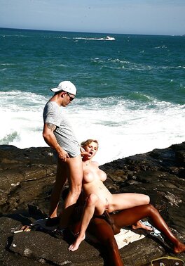 Busty blonde MILF double penetrated on rocky coast by white and black guys