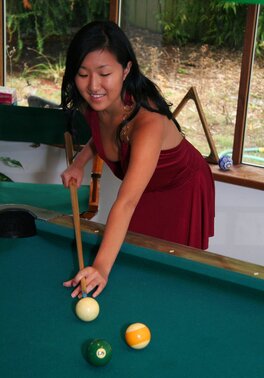 Asian babe in maroon dress climbs the pool table to pose without clothes