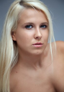 Long-haired blonde demonstrates medium boobs and shaved pussy in the studio