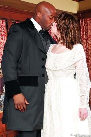 Pale-skinned girl in old-fashioned white dress kisses black man in a suit