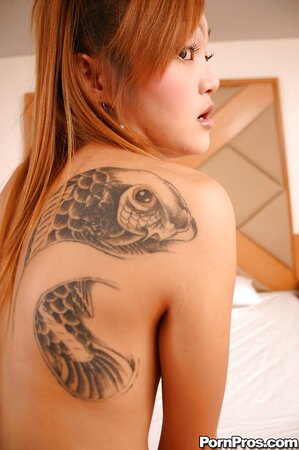 Oriental babe with red hair and tattooed back takes bra and shorts off