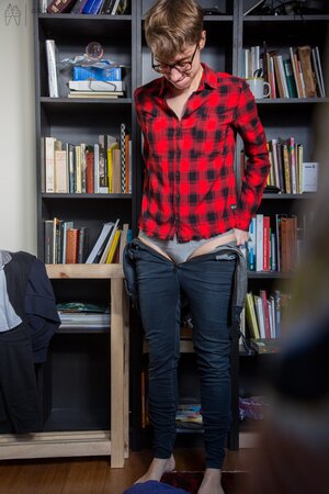 Naked short-haired girl with glasses puts clothes on right in the library
