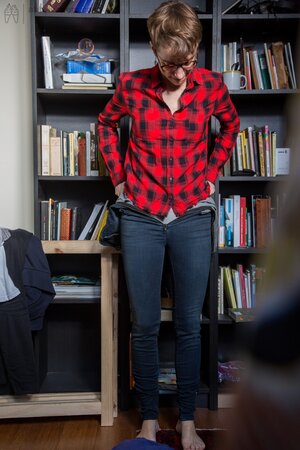 Naked short-haired girl with glasses puts clothes on right in the library