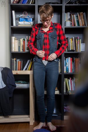 Naked short-haired girl with glasses puts clothes on right in the library