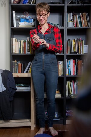 Naked short-haired girl with glasses puts clothes on right in the library