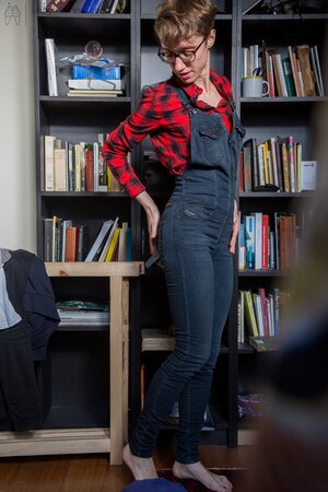 Naked short-haired girl with glasses puts clothes on right in the library