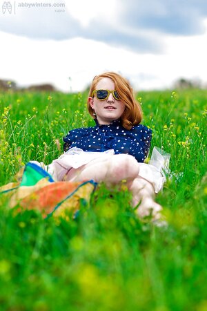 Super-pale ginger lays on the green grass and poses absolutely nude