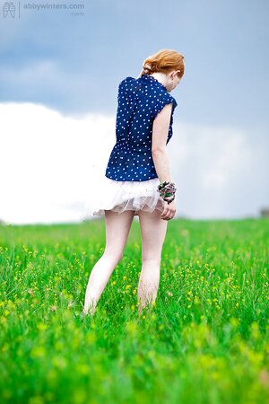 Super-pale ginger lays on the green grass and poses absolutely nude