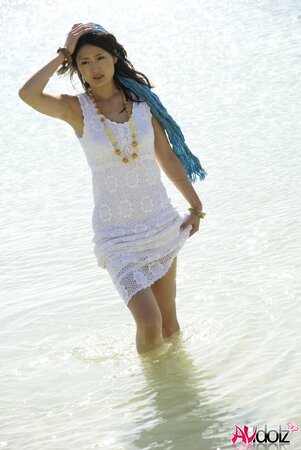 Good-looking Japanese girl in white dress walks into the water being dressed