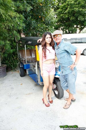 Man in flat cap and sunglasses asks Thai lovely with curly hair to pose on camera