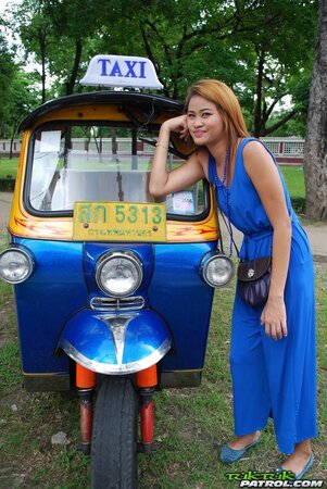 Hot female from Thailand poses in her slinky blue dress by a small taxi
