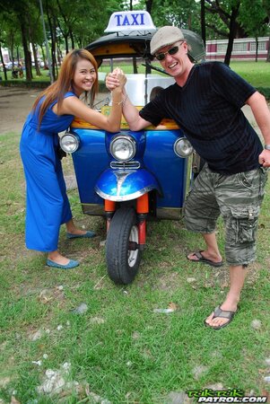 Hot female from Thailand poses in her slinky blue dress by a small taxi