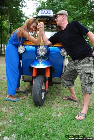 Hot female from Thailand poses in her slinky blue dress by a small taxi