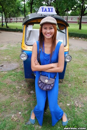 Hot female from Thailand poses in her slinky blue dress by a small taxi