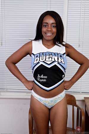 Ebony cheerleader with wonderful natural melons climbs on the table being naked