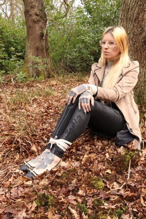 Girl with glasses can't stand up because she is hogtied by the tree