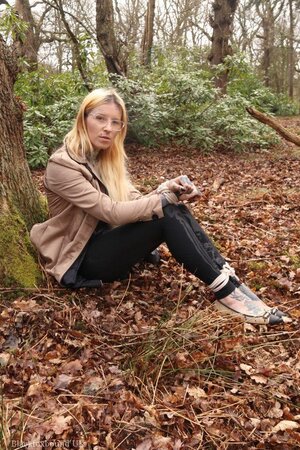 Girl with glasses can't stand up because she is hogtied by the tree