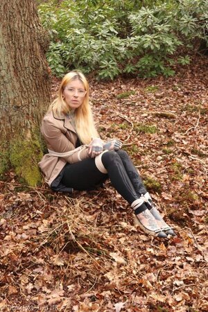 Girl with glasses can't stand up because she is hogtied by the tree