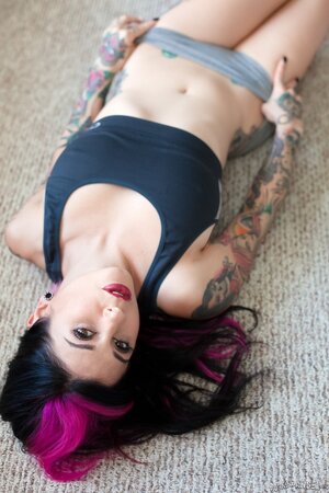 Tattooed woman poses in bedroom in lingerie that accentuates her assets