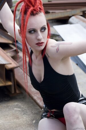 Tattooed emo girl with red dreadlocks poses naked in an industrial zone