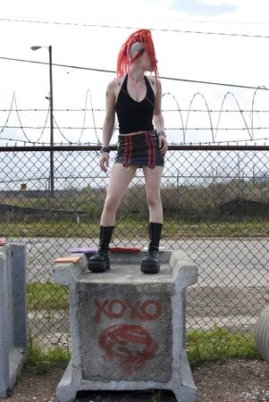 Tattooed emo girl with red dreadlocks poses naked in an industrial zone