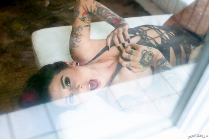 Porn queen strips in front of the glass door and continues posing on the sofa