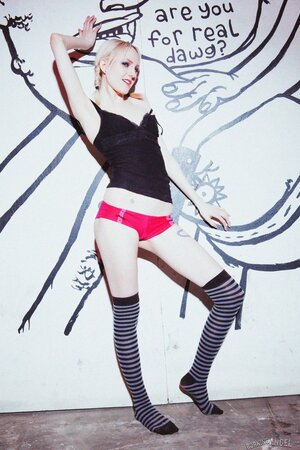 Small-tittied skinny girl in striped over-the-knee socks poses by graffiti wall