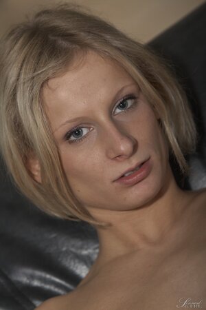 Skinny blonde Paris Pink smiles while posing nude on black leather couch