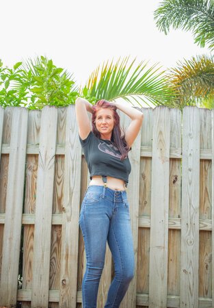 Sexy red-haired MILF takes off everything and poses all naked by the fence