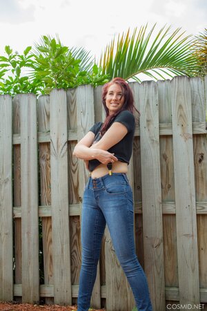 Sexy red-haired MILF takes off everything and poses all naked by the fence