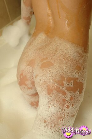 Cutie takes off green swimsuit and covers the body with foam in the bathtub