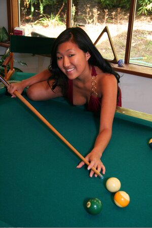 Asian babe in maroon dress climbs the pool table to pose without clothes