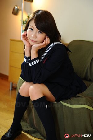 Skinny Eastern female in college uniform smiles so sweet and watches into camera