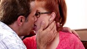 A redhead with glasses is getting pushed and fucked against the sofa